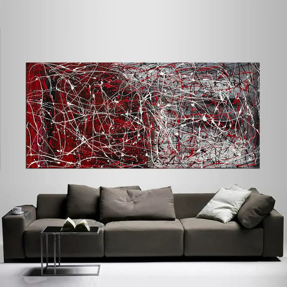 Drip painting on canvas featuring abstract red and gray design, displayed above a modern gray couch in a stylish living room.